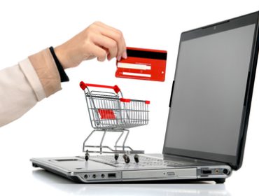 Laptop with small shopping cart and a hand with credit card isolated in white
